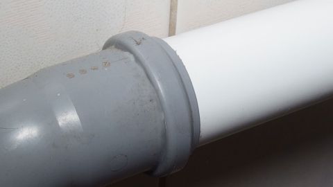 Ein graues Abflussrohr trifft auf ein weißes, das sich nur schwer zusammenstecken lässt, an einer hellen Wand.