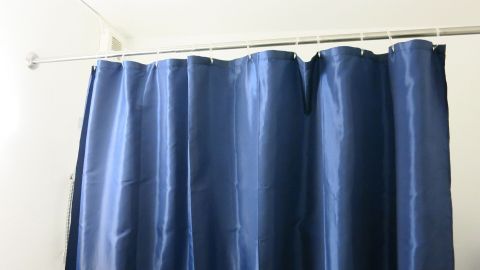Ein blauer Duschvorhang hängt an einer Stange, während im Hintergrund der Raum für das Streichen vorbereitet wird.