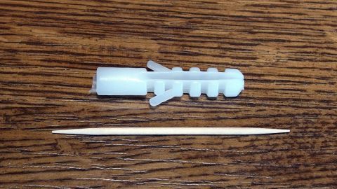 Mithilfe eines Zahnstochers hält der Dübel in einer bröckeligen Wand garantiert dauerhaft. Ein Dübel und ein Zahnstocher liegen auf einem Holztisch, um zu zeigen, wie man in bröckeliger Wand stabilisieren kann.