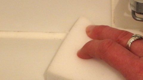 Ein Hand greift einen Schmutzradierer, um Silikon von einer weißen Oberfläche zu entfernen, um sie sauber zu halten.