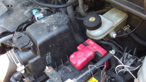 Ein Fahrzeugmotor mit einer roten Batterieabdeckung und einer Bremsflüssigkeitsbehälter, umgeben von Kabeln und Komponenten.