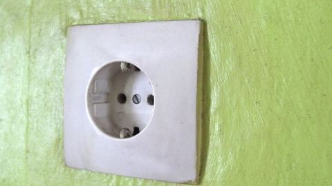 Eine weiße Steckdose ist an einer hellgrünen Wand montiert, bereit zum Überprüfen beim Tapezieren.