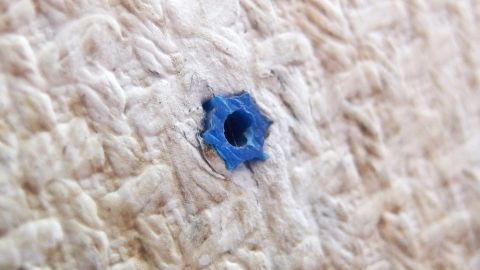 Ein blauer Dübel ist in einem strukturierten, hellen Material platziert, bereit, mit Heißkleber fixiert zu werden.