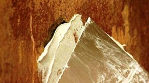 Eine Kelle füllt sorgfältig ein Loch in einer wandbeschichteten Oberfläche mit Spachtelmasse, um es zu reparieren.