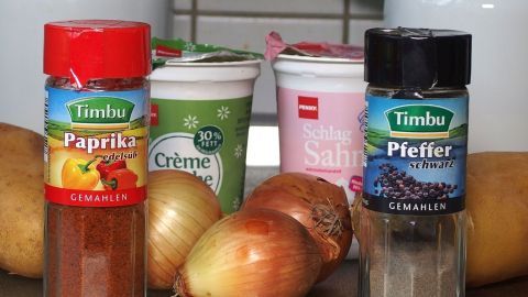 Paprikagewürz und Pfeffer stehen neben Zwiebeln und Joghurt in einer Küchenumgebung, bereit zum Kochen.