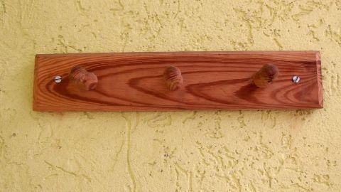 Vermeide Löcher in der Tapete mit cleveren Aufhängelösungen. Nutze Klebehaken oder selbstklebende Schrauben anstelle von Bohrungen, um Ordnung zu schaffen, ohne die Wand zu beschädigen. Ideal für dekorative Holzleisten und mehr. Holzkleiderhaken befestigt an gelber Wand, drei Haken zeigen nach vorne, ideal zum Aufhängen ohne Löcher in der Tapete.