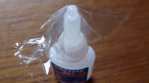 So lässt sich Sekundenkleber beim nächsten Gebrauch wieder öffnen. Ein Fläschchen Sekundenkleber steht auf einem Tisch, während das Verschlussplättchen noch eingesetzt ist und eine Öffnung verhindert.