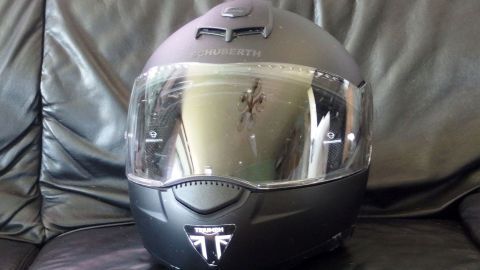 Ein Motorradhelm steht auf einem Lederstuhl, versehen mit Fliegenresten und reflektierender Visieroberfläche.