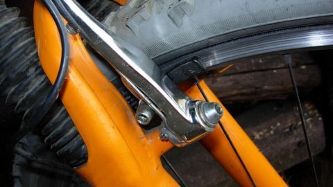 Eine Fahrradfelgenbremse drückt gegen einen Reifen; die orange Gabel zeigt leichte Abnutzungsspuren.