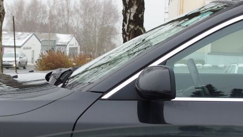 Eine schmutzige Windschutzscheibe eines Autos wird von der Seite aufgenommen, während es in einem verschneiten Umfeld steht.