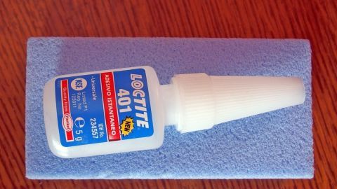Ein Bimsstein liegt auf einem Holzuntergrund, während daneben eine Flasche Sekundenkleber deutlich sichtbar ist.