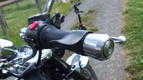 Ein Lenkergriff ist am Motorrad montiert, während die Umgebung aus einem schmalen Weg und grünem Gras besteht.