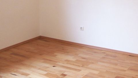Kleine Löcher im Laminat oder Parkett kann man mit Sägemehl und Holzleim ausbessern! Ein Holzfußboden in einem lichtdurchfluteten Raum, bereit für Reparaturen mit Sägemehl und Holzleim.