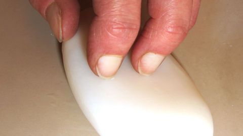 Eine Hand reibt mit einem weißen Seifenstück über eine glatte Oberfläche, um ölverschmierte schwarze Hände schnell zu reinigen.