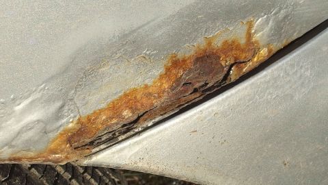 Ein beschädigter Lackbereich an einem Auto zeigt Rost und Verfärbungen, was potenzielle Lackschäden beim Autokauf verdeutlicht.