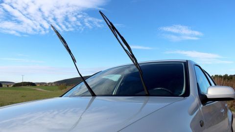 Um Aufkleber von Autoscheiben einwandfrei zu entfernen, ist es ausreichend, ein Stanleymesser mit etwas Nitroverdünnung zu verwenden. Eine Windschutzscheibe mit Wischern, die sich in einer waagerechten Position befinden, steht vor einem blauen Himmel.