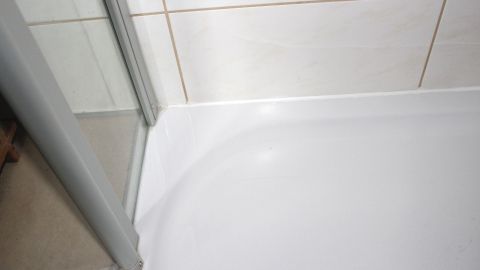 In einer Dusche sind neu hergestellte Silikonfugen sichtbar, die den Übergang zwischen der Duschwanne und den Fliesen abdichten.
