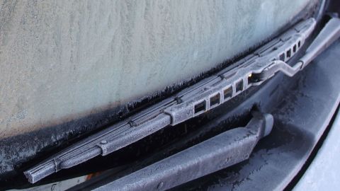 Scheibenwischerblätter liegen auf einer vereisten Windschutzscheibe, betonen die winterliche Kälte in einem Parkplatzumfeld.