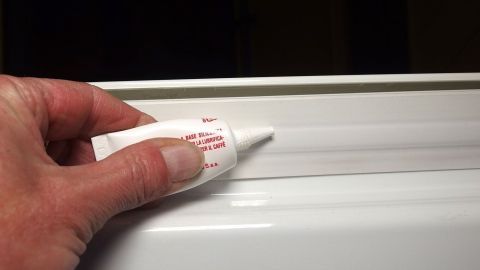 Eine Hand trägt Silikonfett auf die Gefrierfachklappe auf, um das Festfrieren zu vermeiden.