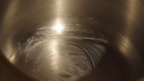 Mithilfe einer Fettschicht am Boden des Topfes, Pudding ohne Anbrennen kochen. Ein Topf mit einer glänzenden Fettschicht im Inneren, bereit zum Puddingkochen ohne Anbrennen, steht auf einer hellen Arbeitsfläche.