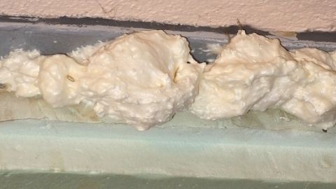 Frisch auf die Haut gelangter Bauschaum kann mit richtig viel Hautcreme oder Körperlotion gut entfernt werden. Bauschaum liegt unordentlich auf einer Fläche, möglicherweise beim Einsatz im Bau, und benötigt Reinigung von der Haut.