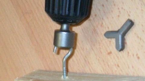 Bohrmaschine dreht Schraubhaken in ein Holzbrett ein, daneben liegt ein kleiner Schlüssel auf hellem Holztisch.