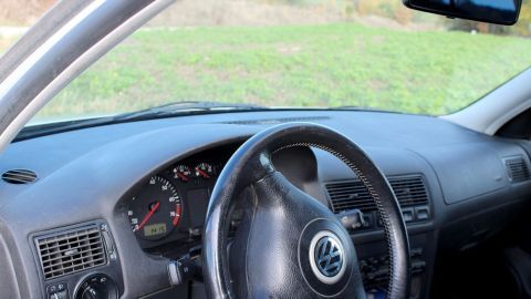 Das Lenkrad eines Autos wird gepflegt, w&auml;hrend es vor einer gr&uuml;nen Wiese geparkt ist, was f&ouml;rderlich f&uuml;r Kunstoff-Armaturen ist.