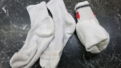 Drei weiße Socken liegen chaotisch auf einer dunklen, marmorierten Oberfläche, zwei sind kurz, eine hat einen bunten Rand.