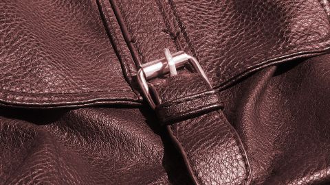 Ein brauner Lederartikel mit einer Metallschnalle liegt locker auf einer Oberfläche und wirkt gut gepflegt.