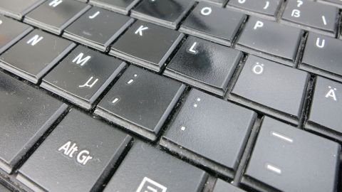 Eine schwarze Tastatur zeigt deutliche Spuren von Flüssigkeitsschaden auf den Tasten, die immer noch in Funktion sind.