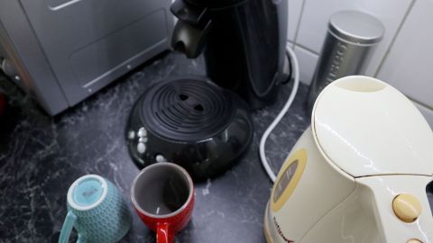 Kaffeekocher und Tassen stehen auf einer Arbeitsfläche in der Kaffeeküche, neben einem Wasserkocher und einer Kaffeedose.