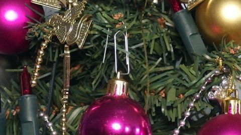 Bunte Weihnachtskugeln hängen an einem Tannenbaum, gesichert mit Büroklammern, um eine festliche Atmosphäre zu schaffen.