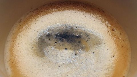 Dunkle Haare werden in einer Tasse mit Kaffee gespült, während sich der Schaum um den Rand bildet.