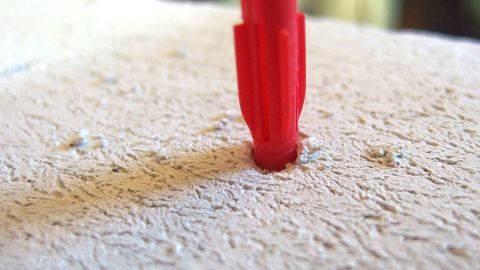 Ein Schrank oder Borte soll für schwere Lasten aufgehängt werden? So gelingt es. Ein roter Dübel wird in ein Loch in einem Gasbetonstein eingesetzt, um eine stabile Befestigung zu gewährleisten.