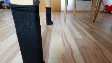 Ein Tisch mit schwarzen Socken an den Beinen steht auf einem hellen Holzboden in einem Wohnraum.