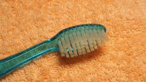 Zahnbürste wird wieder frisch: Zahnbürste zwischendurch mit Gebissreiniger reinigen. Eine Zahnbürste mit weichen Borsten liegt auf einem orangefarbenen Handtuch, bereit für die hygienische Zahnreinigung.