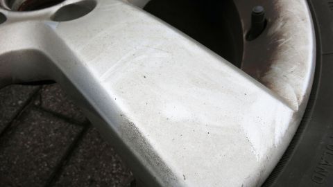 Alufelgen werden gereinigt, während eine Zahnbürste und Essig sichtbar sind; der Hintergrund besteht aus einem gepflasterten Boden.