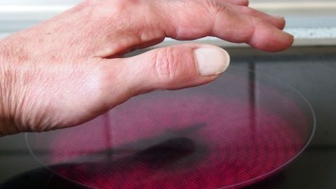 Eine Hand schwebt über einer rot erleuchteten Kochfläche, um Knoblauchgeruch beim Kochen schnell zu entfernen.