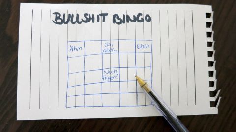 Eine Bingo-Karte mit dem Titel "Bullshit Bingo" und einem Stift zeigt leere Felder auf einem Tisch.