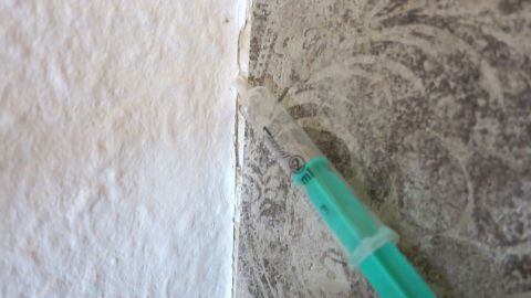 Eine grüne Spritze zeigt eine lockere Stelle in der Tapete, die Beulen aufweist, an einer Wand zwischen zwei Oberflächen.