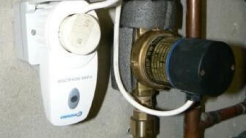 Eine Warmwasserpumpe zirkuliert effizient in einem Heizungsraum; umgeben von gedämmten Rohren und einem Steuergerät.
