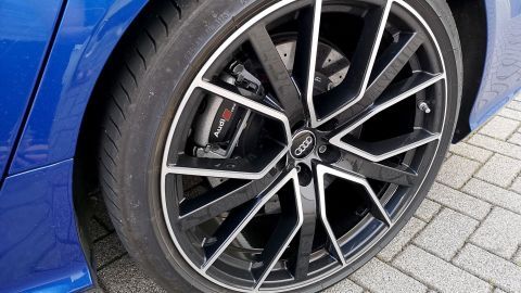 Ein Audi-Autoreifen mit glänzender Felge steht auf grauem Pflasterstein, zeigt klare Details der Bremsanlage und Felge.