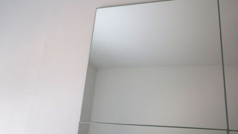 Eine glatte Spiegelfliese ist an einer weißen Wand angebracht, zeigt einen klaren Spiegelblick im Raum.