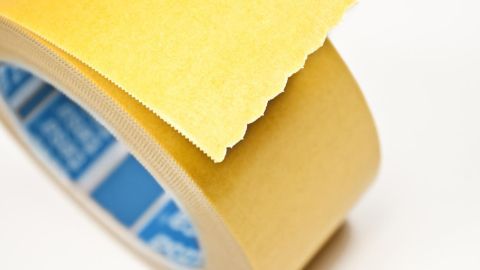 Teppichklebeband, teilweise abgerollt, liegt auf weißem Hintergrund und zeigt seine gelbe Klebeseite.
