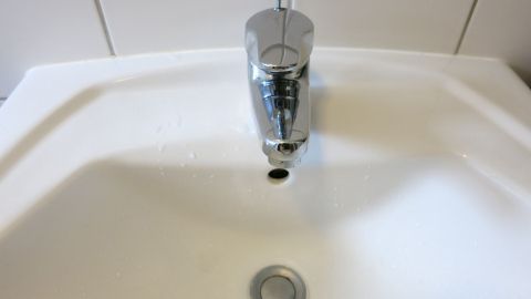 Ein Waschbecken mit einem Stöpsel im Abfluss wird aus der Nähe betrachtet, während Wasser darunter steht und abfließt.