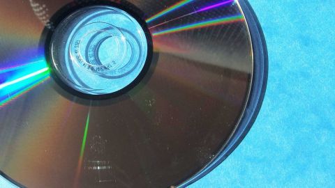 Eine zerkratzte DVD liegt auf einem blauen Untergrund, zeigt deutlich die Kratzer und reflektiert farbige Lichtstrahlen.
