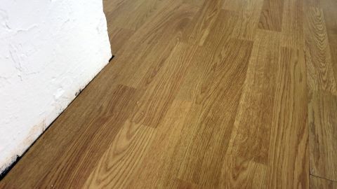 Ein hellbraunes Laminat, das an einer Wand verlegt ist, zeigt Abnutzungsspuren, die nachgefärbt werden könnten.