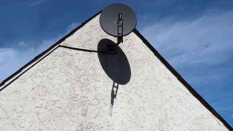 Eine Satellitenschüssel ist an einem weißen Hausdach montiert und empfängt Signale bei klarem Himmel.
