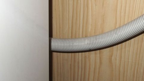 Eine Waschmaschine mit einem grauen Ablaufschlauch, der hinter einem Holzpaneel verläuft, lässt Wasser sofort ablaufen.