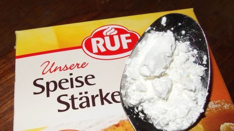 Eine Packung Speisestärke liegt neben einem Löffel mit Pulver, geeignet zum Entfernen von Fettflecken an der Wand.